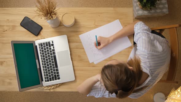 A girl in pajamas remotely learns by writing down a lecture on paper alt
