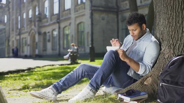 University Student Sitting Under Tree on Campus, Solving Task in Notebook, Smart alt