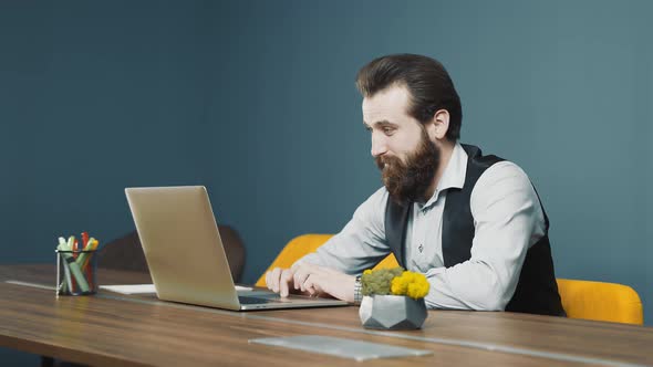Happy Young Man Laughing While Working on Laptop A Man Sitting at a Computer in the Office and alt
