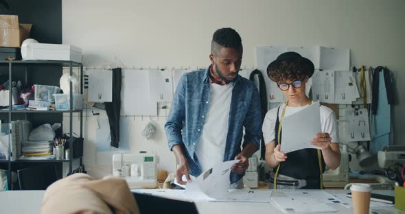 Modern Dressmakers Man and Woman Mixed Race Team Talking Looking at Papers alt