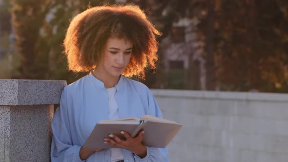 Afro American Woman Young African Girl Student Reads Book Sitting on Street Outdoors in Sun Lights alt