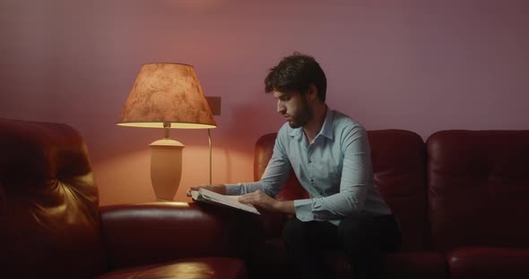 Boy reads a book sitting on the red sofa at home alt