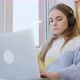 Young woman sitting by the window at home in headphones, working on a laptop. It&#39;s snowing outside. - VideoHive Item for Sale