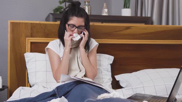 Upset ill Young Brunette Sitting in Bedroom Bed with Scarf Around Her Neck Talking on Phone alt