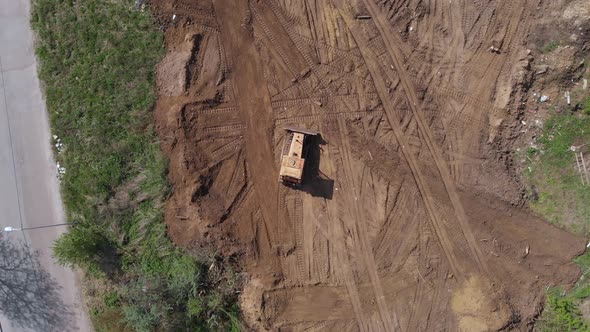 Top aerial view of bulldozer driving on further construction site