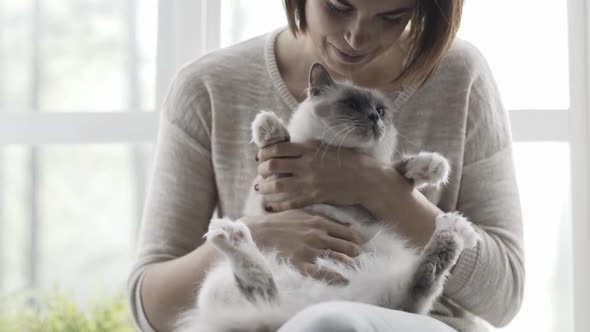 Woman holding and petting her cute cat next to a window