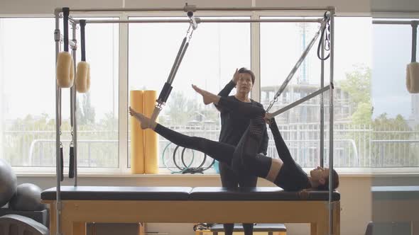 Professional Personal Coach Controls Training of Young Slim Woman in Gym. Wide Shot Side View of alt