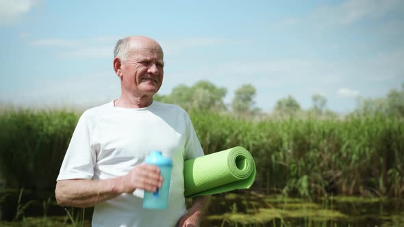 Portrait of Old Man with Rug for Yoga or Meditation in Hands To Take Care of Health and Drink Clean alt