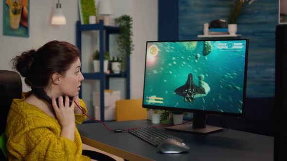 Focused Woman Gamer Sitting on Desk Putting on Headset alt
