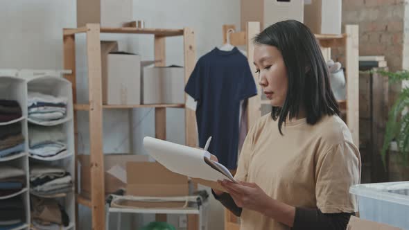 Asian Volunteer Writing in Clipboard while Sorting out Donations alt