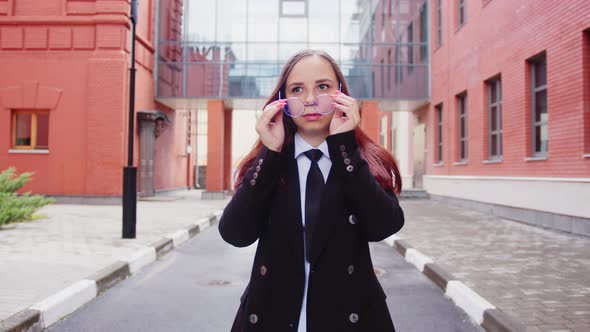 Young Woman in Business Suit Puts on Glasses on City Street alt