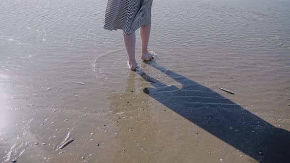 A Woman in a Flowing Dress Enters the Ocean on a Windy Sunny Day