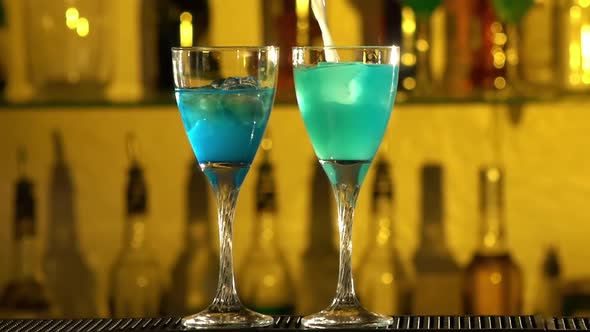 Barman Puts Cubes of Ice Into a Glass, Pouring Three Different Alcohol Liquids, Turquoise alt
