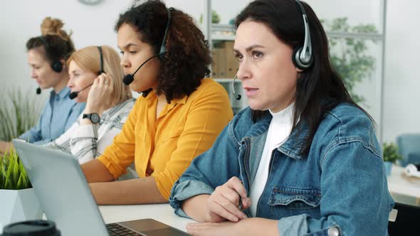 Multiracial Group of Call Center Employees Talking with Headset Typing with Laptop and Taking Notes alt