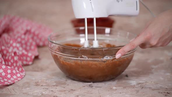 Mixer beating chocolate batter in bowl. alt