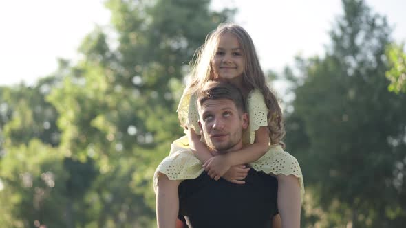Front View Satisfied Girl on Shoulders on Young Man Talking Smiling Standing in Sunshine Outdoors alt