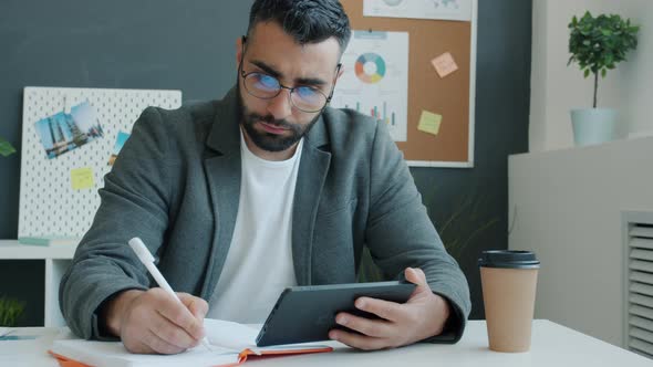 Ambitious Businessman Writing Looking at Tablet Screen Working in Office Room Alone alt