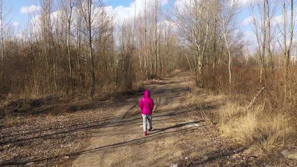 A Girl in a Tracksuit and a Bright Warm Jacket is Walking in the Forest