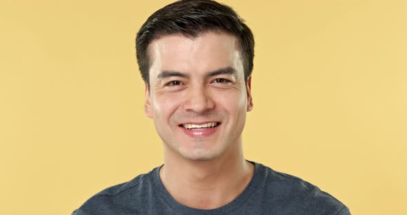 Handsome smiling Hispanic man face in isolated light yellow studio background