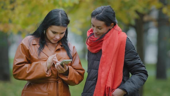Two Hispanic Girls Stand in Autumn Park Using Telephone Women Ordering Food Taxi in Mobile alt