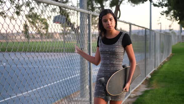 A beautiful young hispanic woman walking through an urban city park with her skateboard along a chai alt