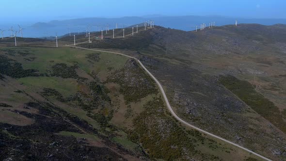 Aerial Over Access Road Leading To Spinning Windfarm Turbines In Hillside Of Galicia In Spain. Dolly alt