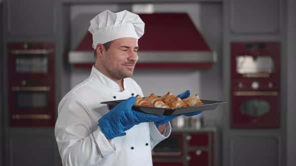 Male Cook Smelling Fresh Croissants Standing in Bakery Kitchen alt