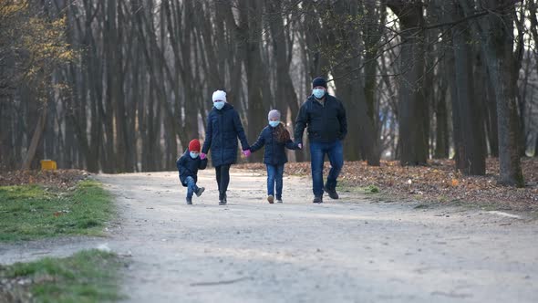 Family: father, mother, son and daughter walk in the Park in medical masks in the spring. 