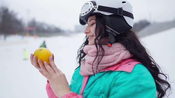 Side View of Happy Beautiful Woman Smelling Healthful Orange in Slow Motion Standing in Snowy alt