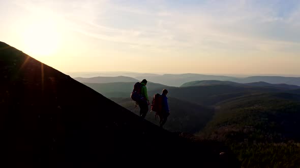 Two Young Hikers with Backpacks Descend a Rocky Ridge at Sunset