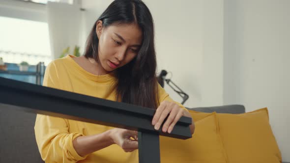 Happy asian young woman unpacking box and reading the instructions to assemble new furniture.