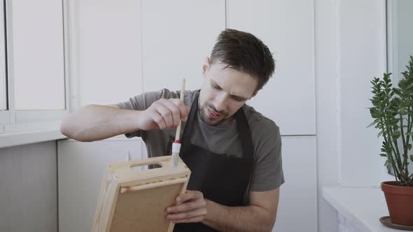Young Craftman in Black Apron Paints Wooden Handmade Box with a White Liquid alt