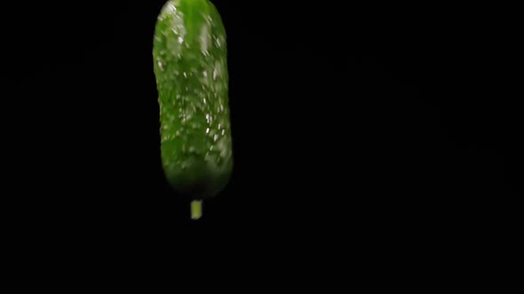 Wet Ripe Cucumber Flies Up and Spinning with Water Splashes on a Black Background in Slow Motion alt