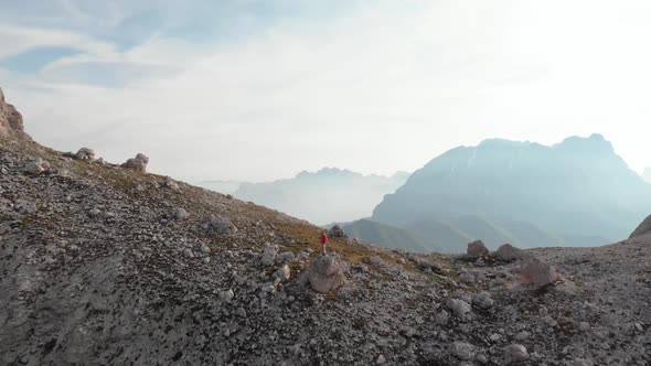 Drone Flying over Man Hiker in Red Jacket Standing on Rock in Dolomites Italy