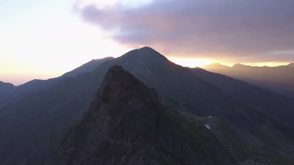 Jagged mountain peak and narrow ridge to summit with dramatic sky and golden light rays streaking ac alt