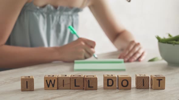 Motivational Message, Slogan I Will Do It Laid Out From Cubes. Young Woman Writes In Notebook alt