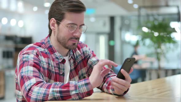 Male Designer Celebrating Success on Smartphone alt