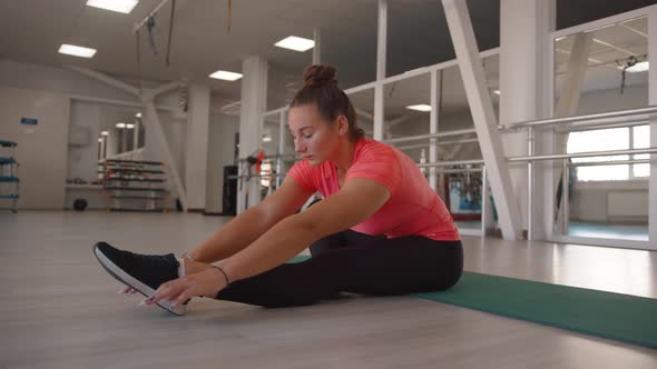 A Beautiful Young Girl Stretches in the Gym and Does Incline to the Leg While Sitting on the Mat alt
