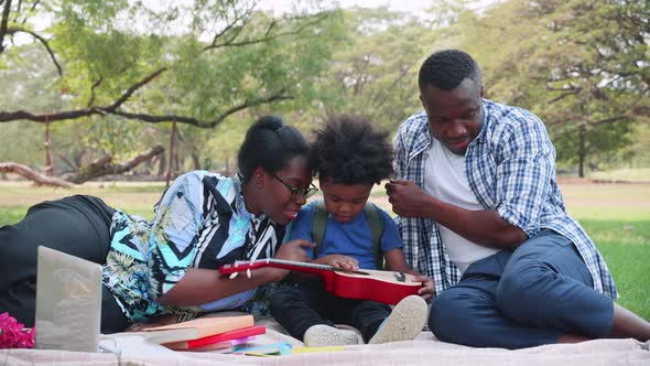 Happy African American Parents teach son play the guitar in the park