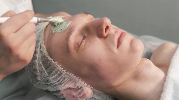 The Hands of the Beautician Applied to the Face with Natural Green Clay