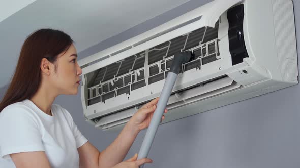 young woman using vacuum cleaner to cleaning the air conditioner at home alt