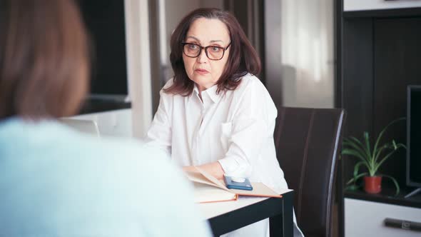 An Attentive Mature Woman Psychologist is Consulting a Patient at Her Office alt