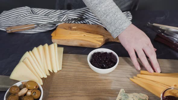 Arranging gourmet cheese, crakers, and fruits on a board for a large cheese board. alt