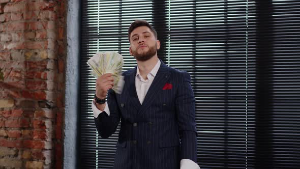 Handsome Young Businessman Holding a Fan Made of Paper Money and Rejoicing in Success alt