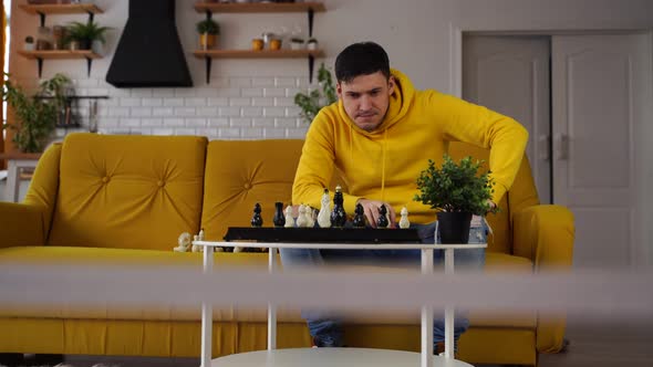 Young Man Sitting on Yellow Sofa and Playing Chess in Room alt