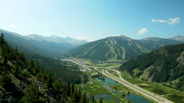 Flying over a mountain peak to see a ski resort and ski runs carved through the pine forest alt