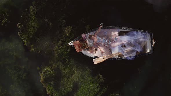 Fantasy Cosplay Concept of Beautiful Princess Woman Relaxing in RowBoat - Overhead Aerial Drone Top  alt