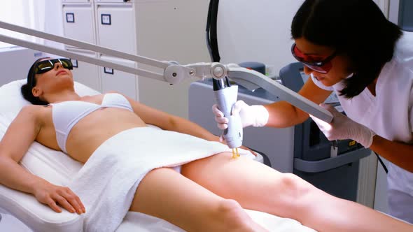 Doctor performing laser hair removal on female patient skin alt