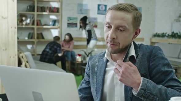 Designer Speaking with Client on Phone and Working on Laptop alt