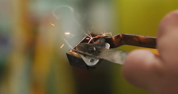 Detail of hand of a Caucasian male factory worker at a factory using a welding gun striker, sparking alt